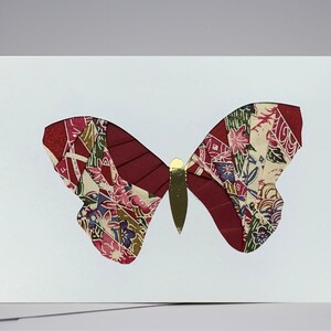 May include: A white card with a red and gold butterfly made of fabric scraps. The butterfly has a detailed pattern of flowers and leaves.