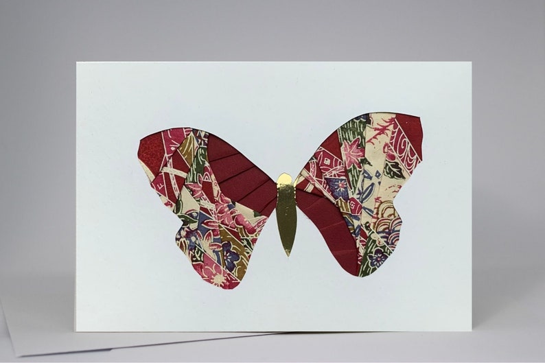 May include: A white card with a red and gold butterfly made of fabric scraps. The butterfly has a detailed pattern of flowers and leaves.