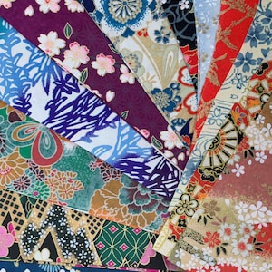 May include: A collection of colorful Japanese washi paper sheets with various floral and geometric patterns. The paper is decorated with gold accents and features a variety of colors, including red, blue, green, and white.
