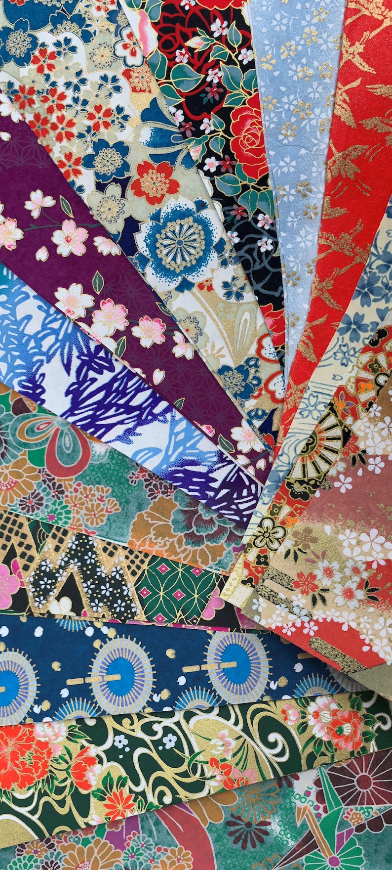 May include: A collection of colorful Japanese washi paper sheets with various floral and geometric patterns. The paper is decorated with gold accents and features a variety of colors, including red, blue, green, and white.