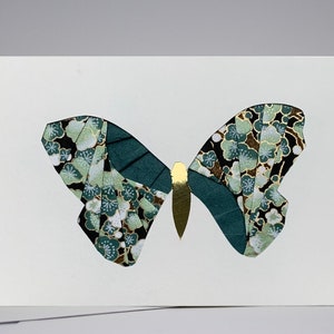 May include: A white card with a green and gold butterfly cut out of patterned paper. The butterfly has a floral design with black, white, and green colors.