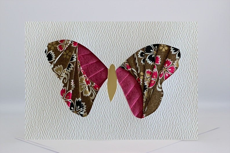 May include: A handmade greeting card featuring a paper butterfly with brown, pink, and gold accents. The butterfly is cut out of the card and has a floral pattern.