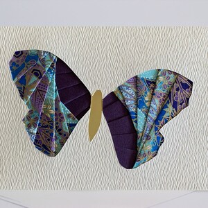 May include: A handmade greeting card featuring a purple and blue butterfly with gold accents. The butterfly is cut out of the card and layered with patterned paper.
