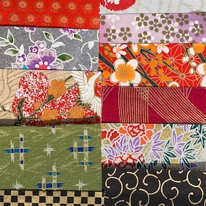 May include: A collection of 18 different patterned Japanese washi paper strips. The strips are arranged in rows and feature a variety of colors, including red, green, blue, gold, and black. The patterns include geometric shapes, flowers, and traditional Japanese designs.