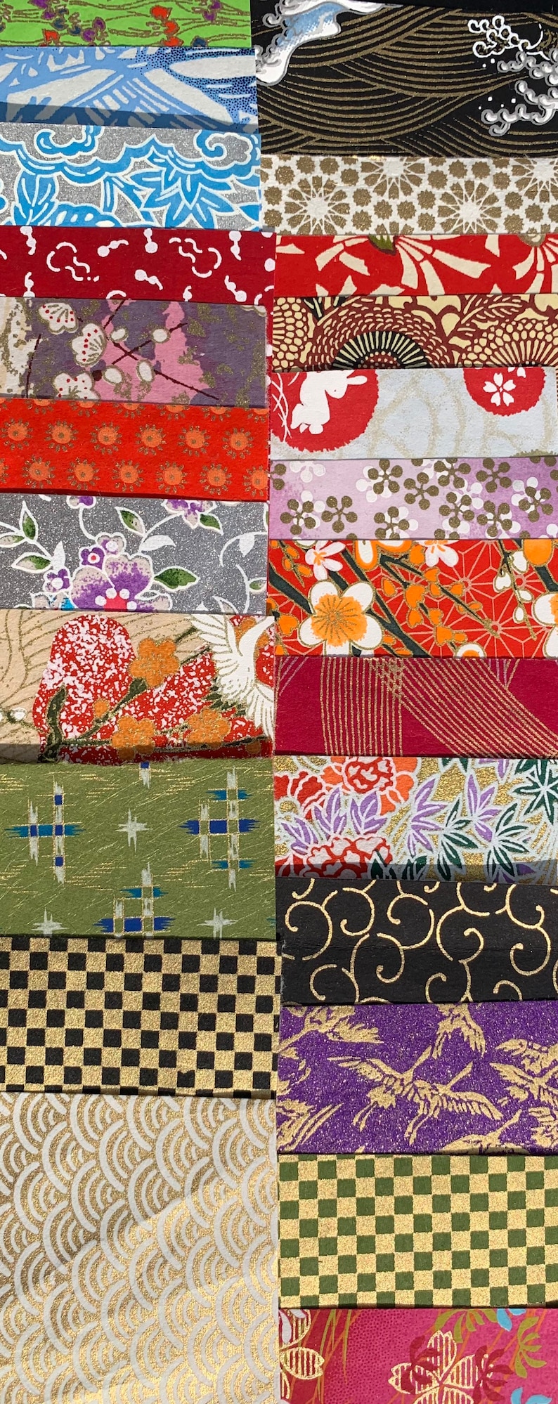 May include: A collection of 18 different patterned Japanese washi paper strips. The strips are arranged in rows and feature a variety of colors, including red, green, blue, gold, and black. The patterns include geometric shapes, flowers, and traditional Japanese designs.