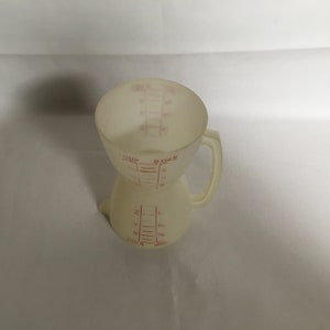 以下が含まれることがあります： オフホワイトのプラスチック製計量カップ。ハンドルと赤い目盛り付き。「1 CUP」と「8 OZS」の表示があります。料理やベーキング用の液体と乾燥材料を測定するように設計されています。