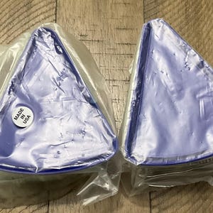 May include: Two triangular, blue plastic trays, each wrapped in clear plastic. The trays are on a wooden surface. One tray has a sticker that says "MADE IN USA".