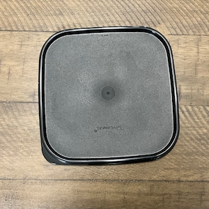 May include: A black round Tupperware container lid with a smooth surface and the word "Tupperware" printed on the bottom.