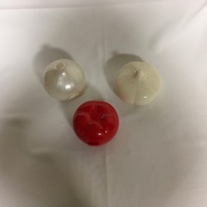 May include: Three kitchen gadgets for storing garlic and onions. One is red, one is white, and one is clear white.