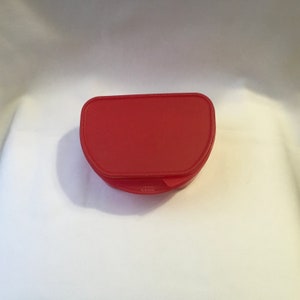 Könnte beinhalten: Ein roter Plastikbehälter mit abgerundeter, gewölbter Oberseite. Der Behälter ist geschlossen und hat eine glatte Oberfläche.