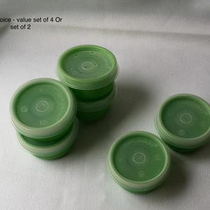 Op de afbeelding: Een verzameling groene plastic containers met witte randen. Sommige zijn op elkaar gestapeld, andere staan los. De tekst in de afbeelding luidt: "Your choice - value set of 4 Or set of 2". Deze containers zijn waarschijnlijk voor voedselopslag.