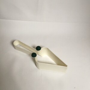 May include: White plastic cake server with two green rubber grips. The server is shaped like a triangle with a curved handle.