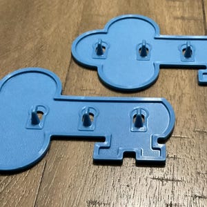 May include: Two blue plastic key-shaped game pieces with four pegs on each. The pieces are designed to be used in a board game.