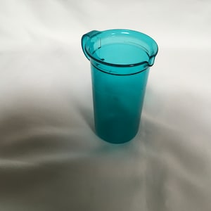 May include: A teal blue plastic pitcher with a handle. The pitcher is empty and has a smooth surface.