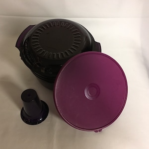 May include: A set of three purple and black plastic containers with a lid, a base, and a small cup. The containers are designed for food storage.