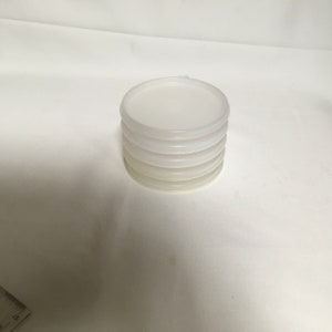 May include: A stack of four white plastic lids for containers.