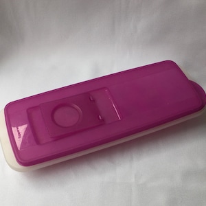 May include: A purple plastic ice cube tray with a white lid. The lid has a small, rectangular cutout for easy access to the ice cubes.