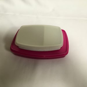 May include: A pink plastic divided container with a white lid. The container is rectangular with rounded edges.