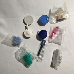 May include: Assortment of kitchen tools and accessories in various colors, including blue, green, white, and pink. The items are packaged in clear plastic bags and include a strainer, a spatula, a lid, and a small container.