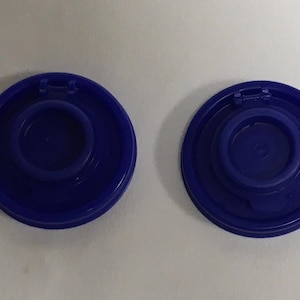 May include: Two blue plastic bottle caps with a raised ring in the center. The caps are designed to fit on top of a bottle.
