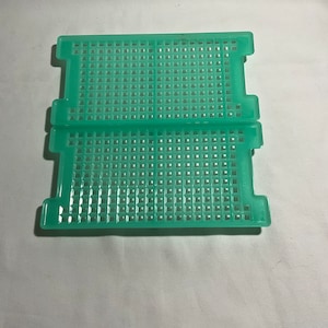 May include: Two green plastic trays with a grid pattern. The trays are stacked on top of each other.