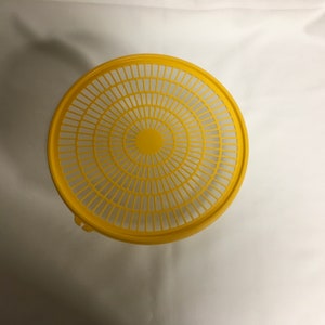 May include: A yellow plastic colander with a circular design. The colander has a handle on the side.