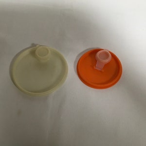 May include: Two round plastic lids, one is white and the other is orange. Both lids have a small, round, clear plastic knob on top.