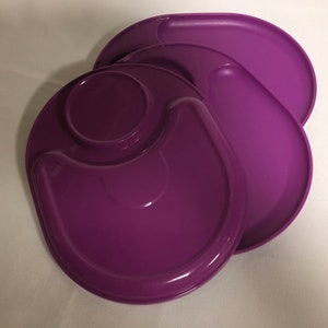 May include: A set of three purple plastic plates with a raised rim and a small indentation in the center. The plates are designed for serving food and are stackable.