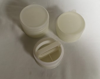 May include: Several stacks of off-white, round, plastic containers with lids. One container has a handle and a divided interior. The containers appear to be new and unused, suitable for storing small items or cosmetics.