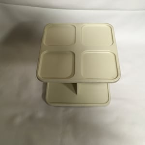 Könnte beinhalten: Ein weißer zweistöckiger Plastik-Organizer mit vier quadratischen Fächern auf der oberen Ebene und einem einzigen Fach auf der unteren Ebene.