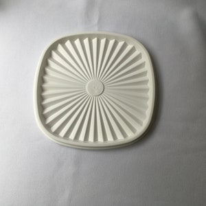 May include: White plastic lid with a circular, textured design in the center. The lid is square-shaped with rounded corners.