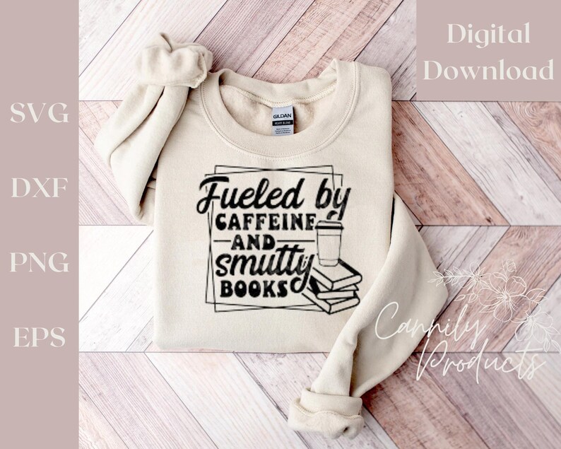 Puede incluir: Una sudadera beige con el texto "Fueled by Caffeine and Smutty Books" en letras negras. El texto est&aacute; rodeado por un marco cuadrado negro. Una ilustraci&oacute;n en blanco y negro de una taza de caf&eacute; y una pila de libros est&aacute; dentro del marco.