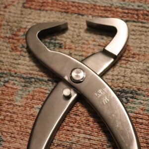 May include: A pair of stainless steel crab crackers with a silver button on the handle. The crackers are designed to crack open crab shells.