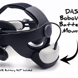 May include: A black VR headset with a white battery mount attached to the side. The text "DAS BoboVR Battery Mount" is written in black marker on a white background. The text "DAS Head Strap and BoboVR Battery NOT Included" is written in black marker on a white background.