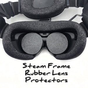 May include: A black virtual reality headset featuring two circular rubber lens protectors inserted over the lenses. The device includes a padded face gasket and adjustable head straps. The text Steam Frame Rubber Lens Protectors is visible.