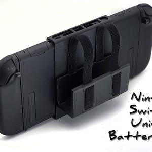May include: A black Nintendo Switch 2 Universal Battery Mount. The mount features adjustable straps and a base designed to securely hold the Switch. The text "Nintendo Switch 2 Universal Battery Mount!" is written in black.
