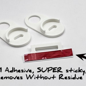 May include: Two white plastic wall mounts with a red 3M adhesive strip. The adhesive is labeled "SUPER sticky, Removes Without Residue".