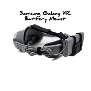 May include: A gray Samsung Galaxy XR Battery Mount with a black strap and a gray power bank attached. The text "Samsung Galaxy XR Battery Mount" is written in black cursive. The mount is designed to hold a power bank for extended use.