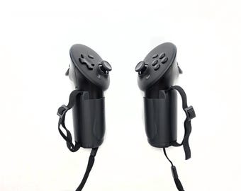 Könnte beinhalten: Ein Paar schwarze Virtual-Reality-Controller mit einem kreisförmigen Oberteil, das ein Steuerkreuz, einen Analogstick und mehrere Aktionstasten enthält. Jeder Controller verfügt über eine verstellbare schwarze Handschlaufe an der Basis.