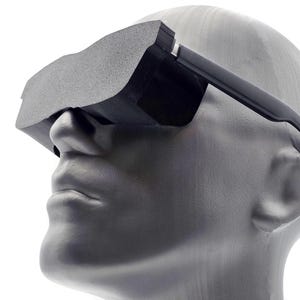 May include: A black virtual reality headset worn on a grey mannequin head. The device features a solid, matte black front panel that covers the eye area, connected to thin, black side arms that extend back along the sides of the head.