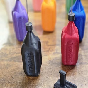 Könnte beinhalten: Ein Satz von acht bunten 3D-gedruckten Flaschen mit einer schwarzen Flasche mit der Aufschrift "Printer Plugger" und einem schwarzen Ständer.