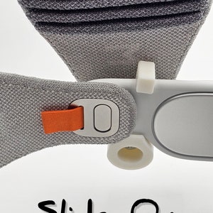 May include: A close-up of a gray and white headband with an orange strap and a silver button. The headband has a slide-on style and the text "Slide-On Style" is written below.