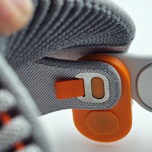 May include: A close-up of a gray and orange headset with a strap and a button. The headset is made of a soft, comfortable material.