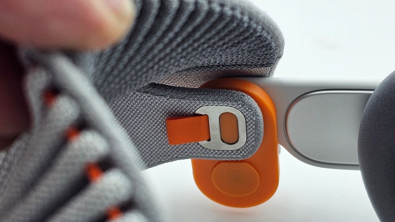 May include: A close-up of a gray and orange headset with a strap and a button. The headset is made of a soft, comfortable material.