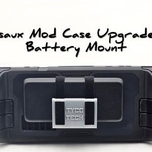 Peut inclure: Une console Nintendo Switch noire avec un étui de protection noir. L'étui est doté d'un support de batterie imprimé en 3D gris avec le texte "TYCO TECH" imprimé dessus. Le support de batterie est fixé à l'aide de sangles noires.