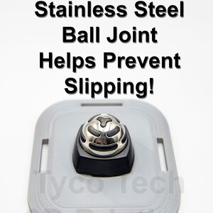 May include: A close-up of a silver ball joint with a black rubber inlay. The ball joint is mounted on a gray plastic base. The text "Custom Rubber-Inlaid Stainless Steel Ball Joint Helps Prevent Slipping!" is printed above the ball joint. The text "(Steel-on-steel versions are too slippery)" is printed below the ball joint.