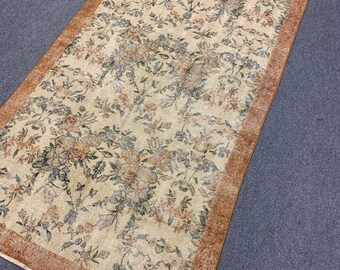 May include: A vintage floral patterned rug with a brown border. The rug has a cream background with a floral pattern in shades of brown, green, and blue.