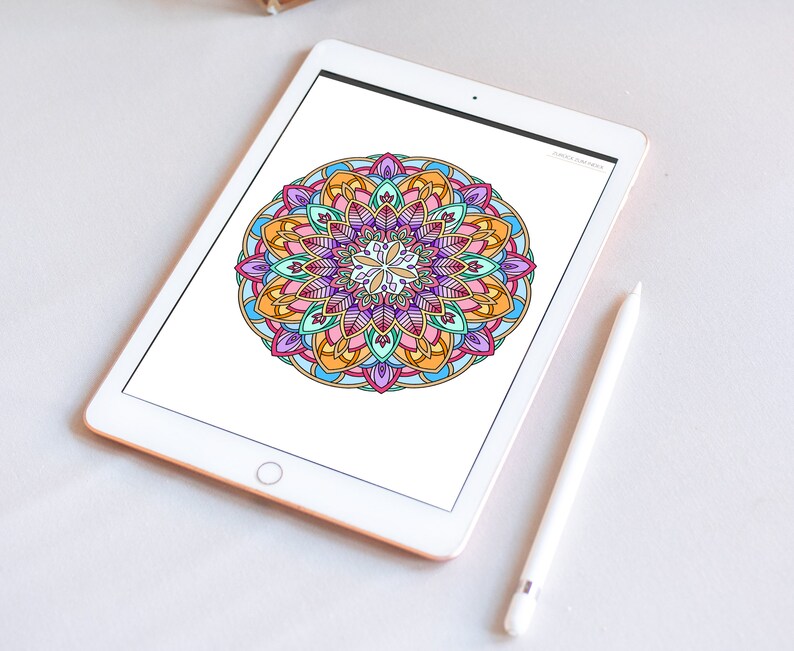 May include: A digital tablet displaying a colorful mandala design with intricate details. The tablet is white with a silver frame and is lying flat on a white surface. A white stylus is lying next to the tablet.