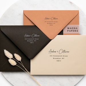 May include: Three envelopes with different coloured paper, each with the same address printed in white: Andrew + Catherine, 335 Greenwich Street, Brooklyn, NY 10013. The top envelope is a light brown colour, the middle envelope is black, and the bottom envelope is a light beige colour. The top envelope has a clear sticker with the text "MAGNA PAPERS" printed in black.