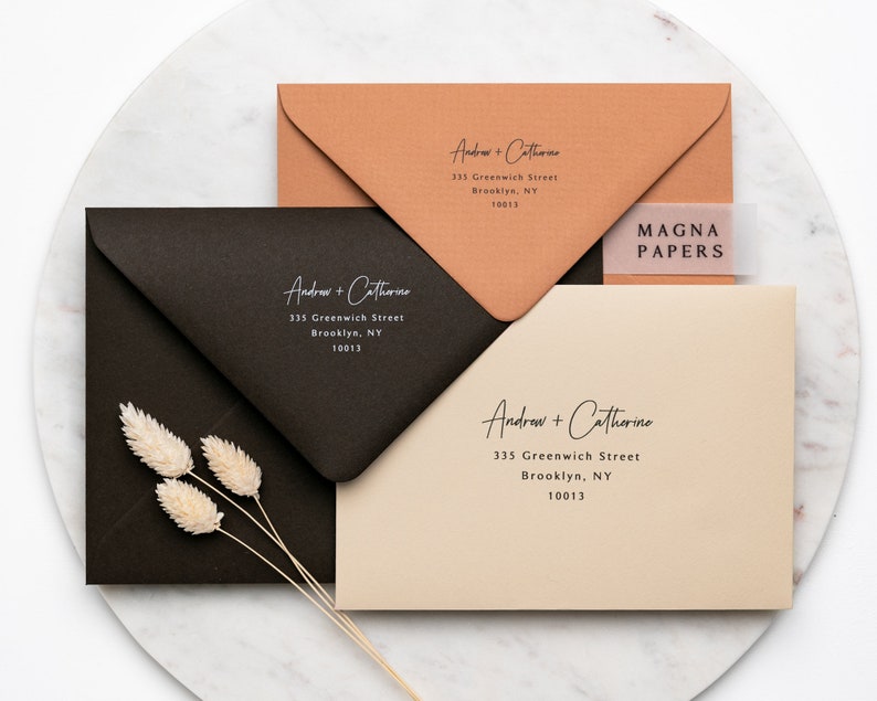 May include: Three envelopes with different coloured paper, each with the same address printed in white: Andrew + Catherine, 335 Greenwich Street, Brooklyn, NY 10013. The top envelope is a light brown colour, the middle envelope is black, and the bottom envelope is a light beige colour. The top envelope has a clear sticker with the text "MAGNA PAPERS" printed in black.